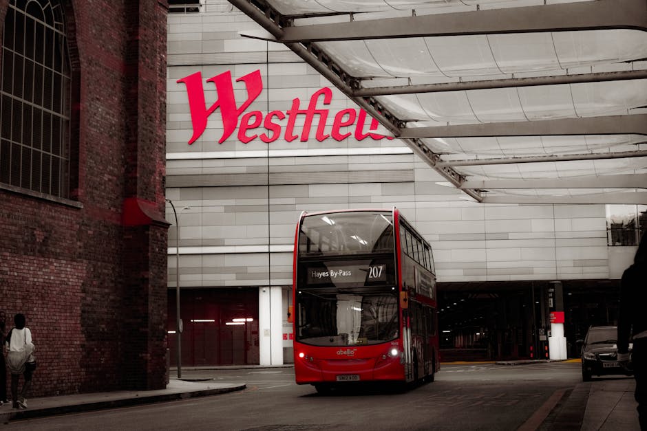 The image depicts a modern, multi-storey commercial building at night, featuring large illuminated signs displaying the words 'Westfield' in red and 'PRIMARK' in blue on the exterior facade. The build